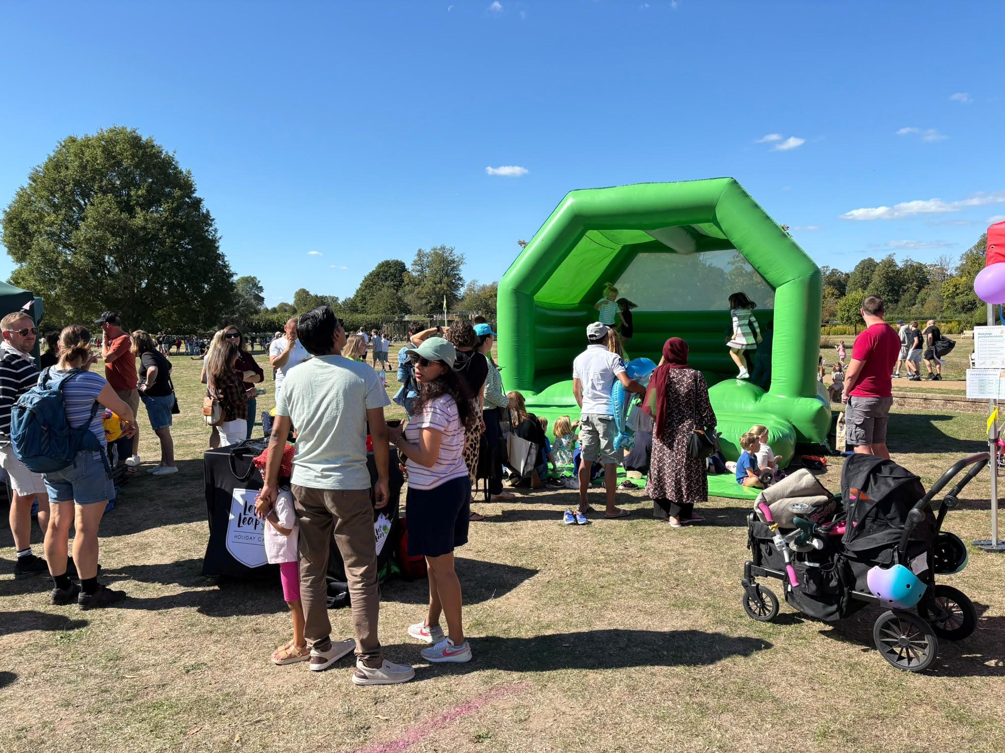 The green bouncy castle in the children’s area, with families watching from the grass and a pushchair in the foreground.