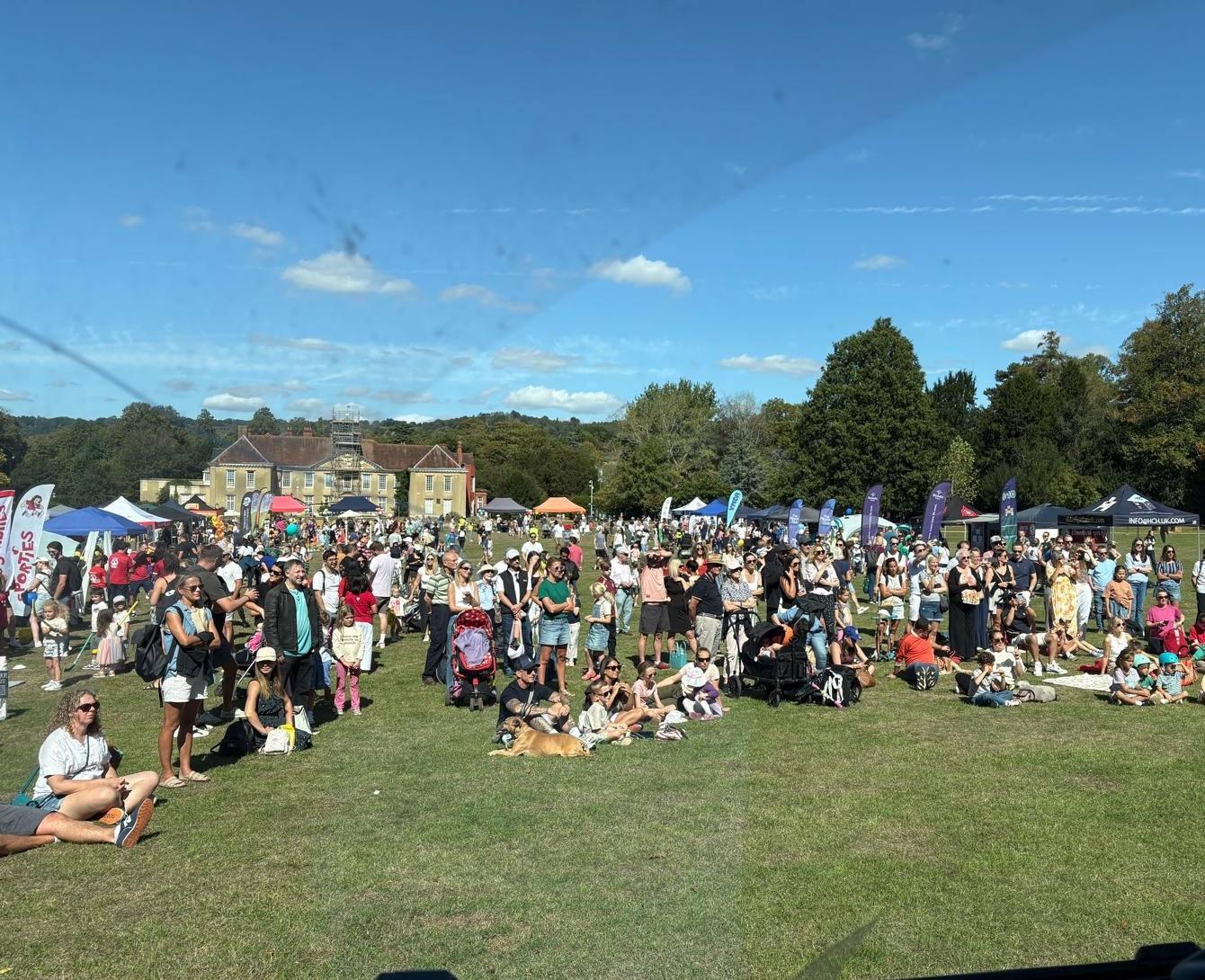 The eastern field of Reigate Priory Park full of families on a clear September afternoon, club gazebos and banners along the far side, the Priory building and the North Downs behind.